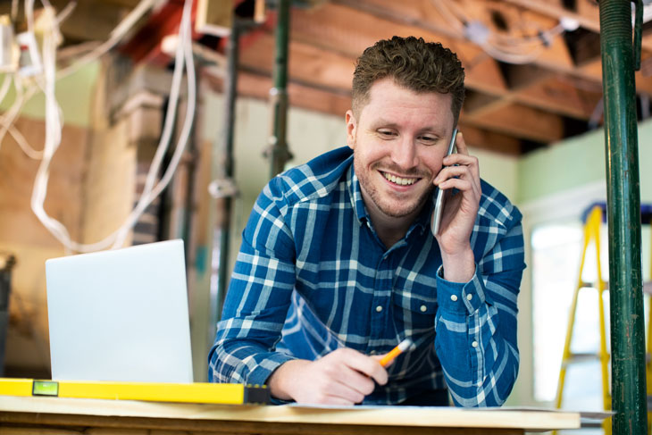 Man on phone next to a laptop in a building under construction. 