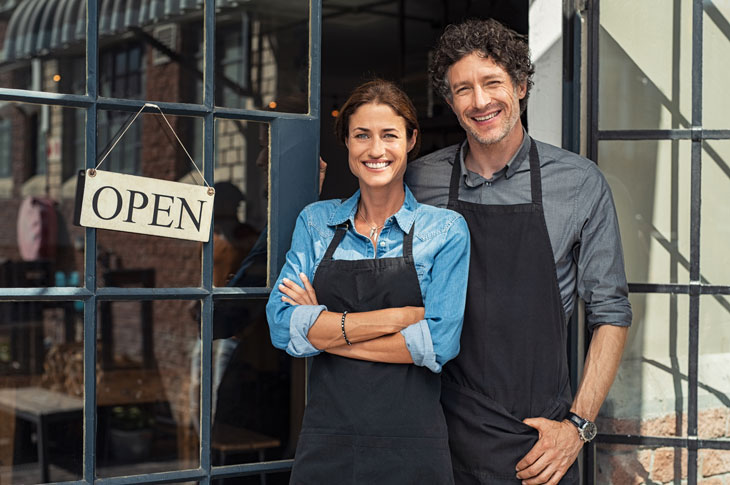 A man and woman in aprons stand smiling next to an 