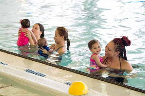 Three moms each holding one small baby in a pool getting ready to teach them to swim/be safe in the water.