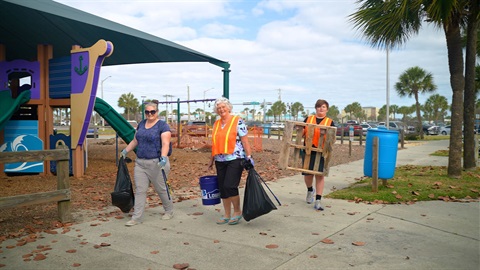 Three Trash Bash volunteers holding bags, buckets and large items of trash at Paradise Beach Park. 