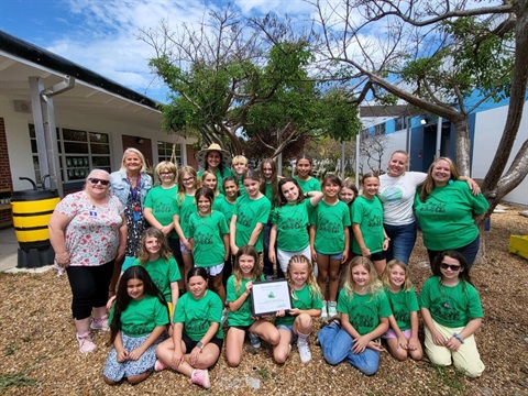 Cheryl Caldwell with group of Indialantic Elementary School students and teachers. All the kids are wearing green Indialantic Elementary School shirts, and two of the girls in front are holding the ECO School Award certificate. 