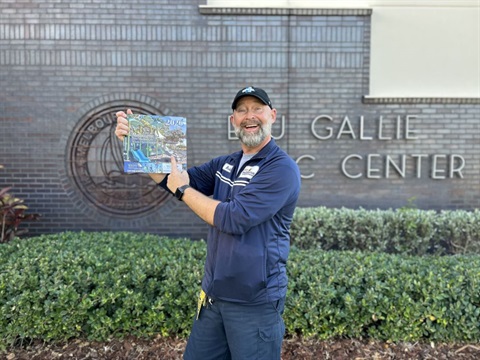 Man smiling and holding  2026 Parks, Recreation and Golf calendar in front of Eau Gallie Civic Center