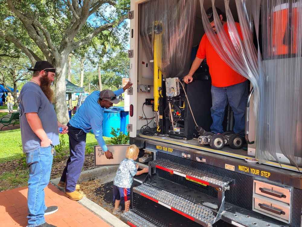 ublic Works employee helps child look inside part of a camera inspection truck
