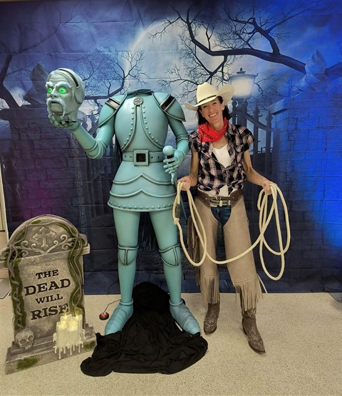 Woman in Halloween costume smiling and standing next to Halloween decorations