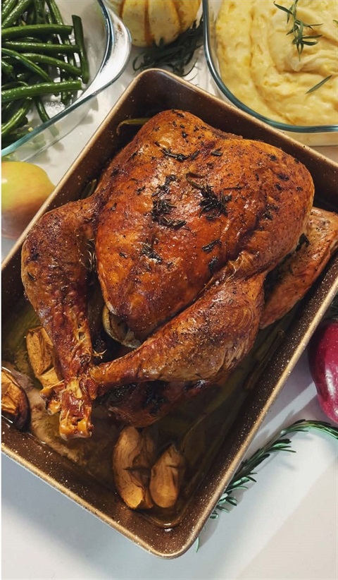 Cooked Thanksgiving turkey in a roasting pan on a table with green beans and mashed potatoes