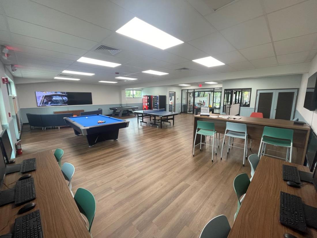 Newly renovated game room at Joseph N. Davis Community Center with computer tables and chairs, pool table, ping pong table, foosball table, vending machines, large screen TV and seating area.