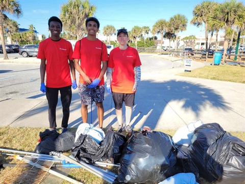 Three trash bash volunteers standing in front of several bags of trash at Paradise Beach Park. 